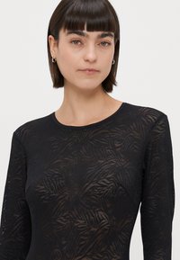 Melna garām piedurknēm tops ar teksturētu lapu rakstu, apaļu kakla izgriezumu un pieguļošu dizainu. Izgatavots no viegla, puscaurspīdīga auduma.