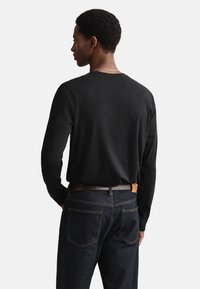 Camiseta negra de manga larga hecha de tela suave, con un cuello redondo clásico. Combinada con jeans azul oscuro y un cinturón de cuero marrón.