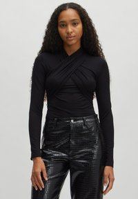 Zwarte lange mouwen top met een kruislings ontwerp, gecombineerd met hoge zwarte neplederen broek met een gestructureerd krokodillenpatroon.