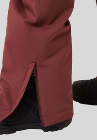 Water-resistant, maroon ski pants with a side zipper and elastic cuff, designed for easy wear over black snow boots.