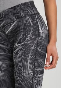 Leggings de patrón negro y gris con una cintura alta. La tela es elástica, con una textura suave y sutiles diseños en forma de círculos en toda su superficie.