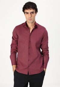Chemise à manches longues bordeaux à boutons avec un motif texturé et un col. Présente une coupe ajustée et des détails de boutons.