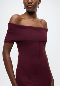 Robe bordeaux épaules dénudées avec une texture côtelée, une coupe ajustée et un décolleté droit, dotée de manches courtes et d'un design corporel lisse.
