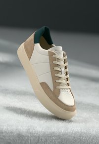 Sneakers da uomo con tomaia in pelle bianca, dettagli in suede beige, colletto verde, lacci piatti e suola in gomma testurizzata color crema.