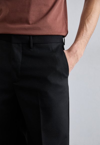 Pantalones negros de corte ajustado con una textura suave, que cuentan con un corte recto, bolsillos laterales y una cinturilla plana. Combinados con una camiseta marrón.