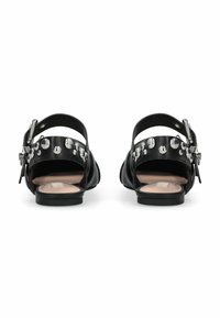 Sandales en cuir noir avec un petit talon. Elles comportent une sangle arrière ornée de grandes clous métalliques et une fermeture à boucle pour l'ajustement.