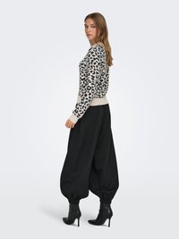 Kreemikas-must lõopardi mustriga kampsun, mida kannavad laiad mustad püksid. Modellil on jalas mustad kõrge kontsaga saapad. Siledad tekstuurid, lõdvestunud istuvus.