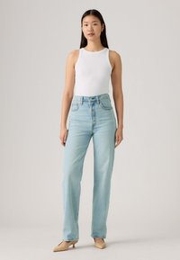 Witte geribde tanktop gecombineerd met lichtblauwe high-waisted wijde jeans. Beige puntige hakken maken de outfit compleet. Eenvoudige, strakke lijnen.