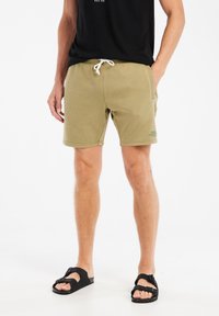 Olijfgroene shorts met zakken, elastische tailleband en witte trekkoord. Gemaakt met zwarte sandalen, wat een casual ensemble presenteert.