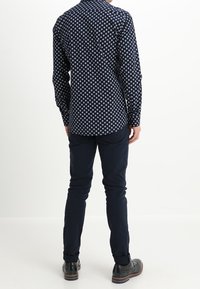 Nachtblauw overhemd met witte stippen; lange mouwen en kraag; gecombineerd met donkere broek en schoenen; gladde stoftextuur.