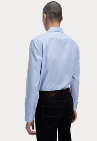 Ljusblå långärmad skjorta med klassisk krage, med knäppta manschetter och en slät textur, i kombination med mörka denimjeans.