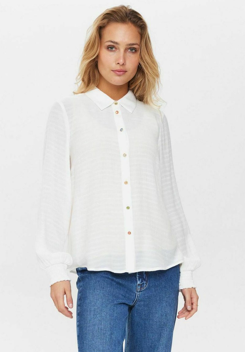 Camicia bianca con chiusura a bottoni, caratterizzata da bottoni colorati, colletto e maniche lunghe a sbuffo. Tessuto leggero e testurizzato.