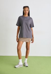 Grå crew neck t-skjorte, beige mini-skjørt, og reflekterende sølv sneakers med hvite sokker. Enkel design, avslappet passform, Nike-logo på plagget.