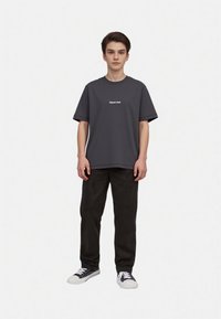 Gray short-sleeved t-shirt with a rounded neckline, featuring white text on the chest; paired with black trousers and black sneakers.