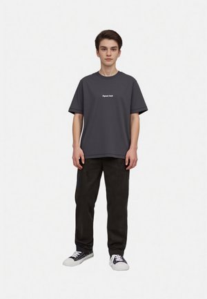 Gray short-sleeved t-shirt with a rounded neckline, featuring white text on the chest; paired with black trousers and black sneakers.