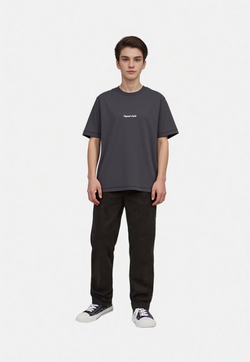 Gray short-sleeved t-shirt with a rounded neckline, featuring white text on the chest; paired with black trousers and black sneakers.