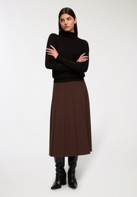 Maglione nero a collo alto, gonna midi plissettata marrone e stivali neri con tacco al ginocchio. Texture lisce e design semplice ed elegante.