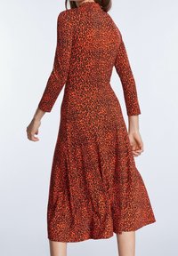 Punainen ja musta leopardikuvioinen mekko, jossa on pitkät hihat, istuva yläosa, levenevä helma ja korkea kaulus. Valmistettu pehmeästä, joustavasta kankaasta.