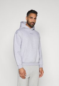 Γκρίζα φούτερ με καγκουρό τσέπη, κουκούλα με κορδόνι και ραμμένα μανίκια. Διαθέτει κεντημένο κείμενο στο στήθος. Ζευγάρι ανοιχτόχρωμων γκρι φόρμες.