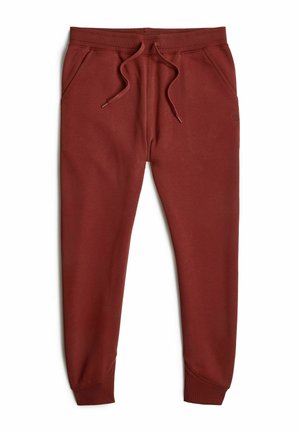 Pantalon de jogging en coton rouge avec une taille élastique et un cordon de serrage, doté de deux poches et de poignets ajustés aux chevilles.