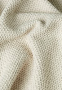 Waffle-textured fabric in off-white, showcasing a soft, woven appearance with raised grids for a tactile finish.