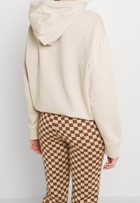 Beige hoodie med kangorufickor och justerbar huva, i kombination med bruna och beige rutiga leggings, som framhäver en avslappnad stil.