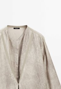 Cardigan gris clair en tissu doux et texturé, doté d'un col en V, d'une patte de boutonnage avant minimaliste et d'accents contrastants beige clair sur les épaules.
