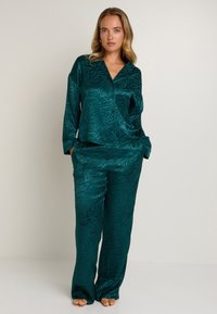Ensemble de pyjama en satin teal avec un motif zèbre subtil, comprenant un haut à col et un pantalon à coupe décontractée, texture lisse et détails de boutons.