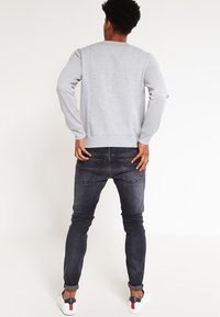Felpa grigia con maniche lunghe, scollatura rotonda e orlo a costine, abbinata a jeans di jeans scuri e sneakers bianche con dettagli blu navy e rossi.