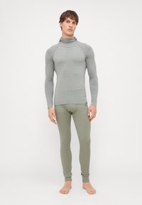 Un haut à manches longues gris côtelé avec col roulé et un pantalon vert ajusté. Les deux sont en tissu lisse, avec des textures subtiles et un branding minimal.