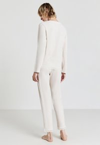 Pigiama in crema chiaro realizzato in morbido tessuto; top a maniche lunghe e pantaloni lunghi con dettagli a bordo ondulato. Superficie testurizzata, vestibilità casual.