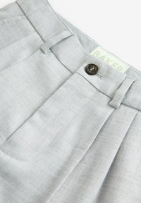 Pantaloni grigi chiari su misura con chiusura a bottone, fronte plissettato e texture liscia con un sottile motivo tessuto.