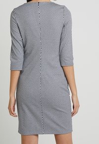 Upnuté šaty v monochromatických tónech s geometrickým vzorem, tříčtvrteční rukávy a zadní zip. Hladká tkanina s mírným leskem.