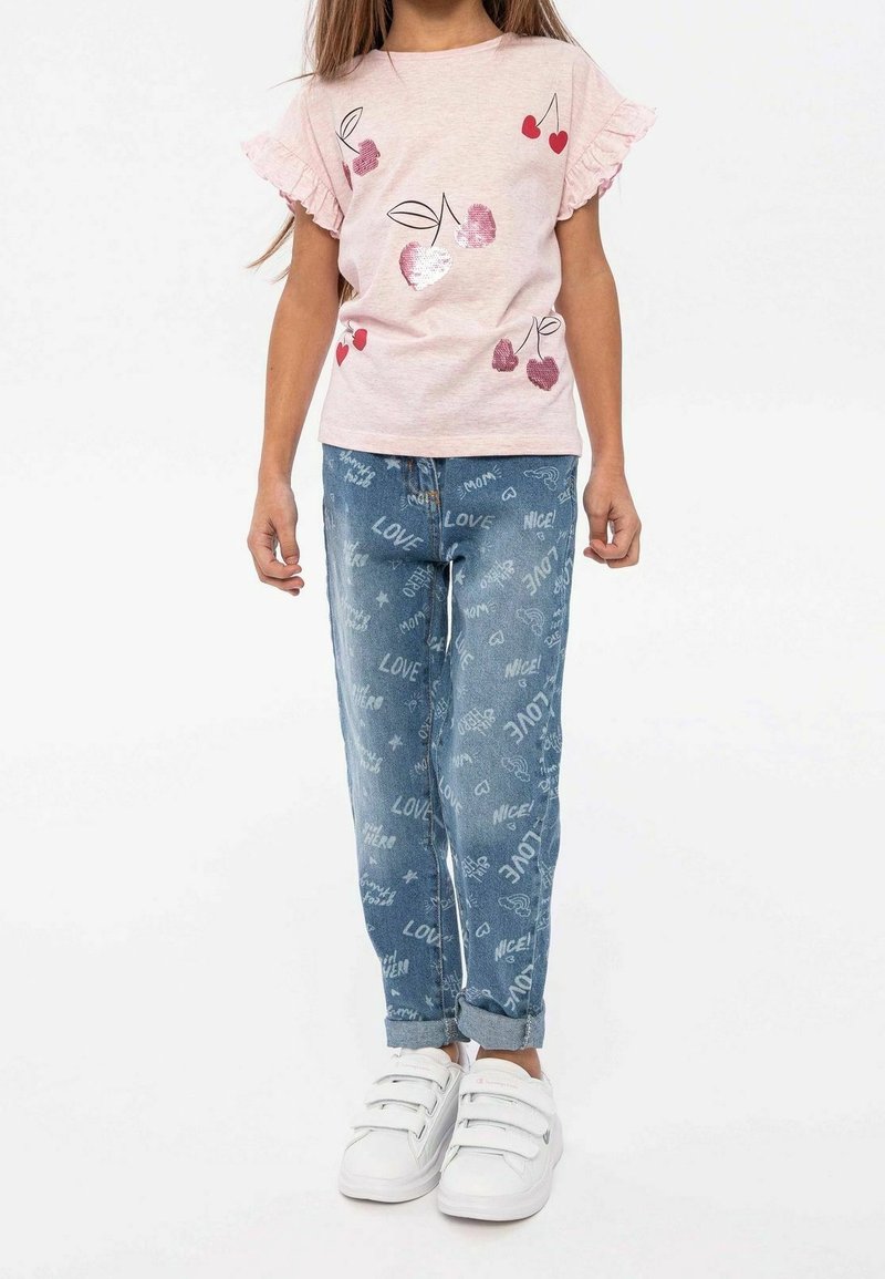 T-shirt rose clair avec des manches volantes et un motif de cerise ; jeans en denim bleu avec un motif "love" ; baskets blanches avec des straps en Velcro.