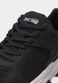 Μαύρο sneaker Just Cavalli με διχτυωτά πάνελ, χονδρές μαύρες κορδόνια και λευκή υφασμένη σόλα.