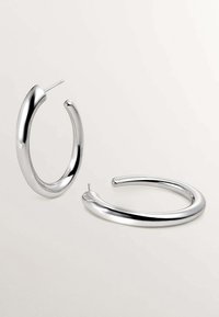 Pendientes de aro de plata con una superficie lisa y reflectante y un diseño abierto y redondeado; cuenta con un respaldo tipo poste para un ajuste seguro.