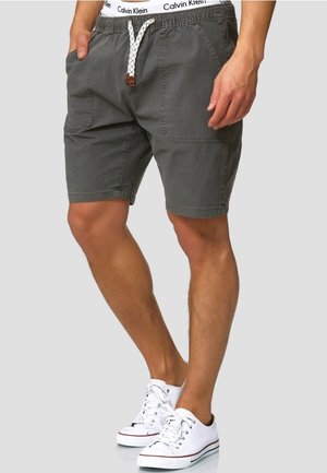 Shorts gris foncé avec une coupe décontractée, dotés de poches latérales, d'une taille avec cordon de serrage et d'un tissu texturé. Portés avec des baskets blanches.