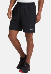 Pantalones cortos deportivos negros con cinturilla elástica y bolsillos laterales. Presenta un logo blanco de FILA en el lado izquierdo. El material parece liviano.