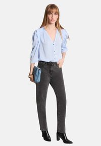 Blusa azzurro chiaro con maniche a sbuffo e bottoni, abbinata a jeans neri dritti grigi scuri e stivaletti neri; tiene in mano una pochette blu.
