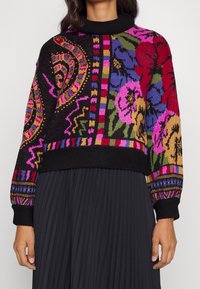 Gehaakte trui met een zwarte basis en meerkleurige bloem- en geometrische patronen, een geribbelde kraag en lange mouwen met contrasterende manchetten.