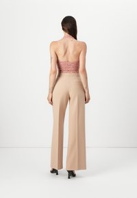 Brown and pink halter crop top paired with high-waisted, light beige wide-leg trousers. Smooth texture with minimal detailing.