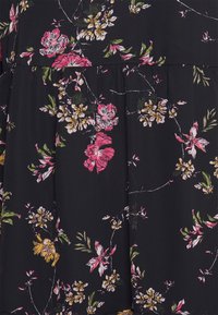 Un tissu noir présente un motif floral avec des fleurs roses et jaunes. Le design inclut des feuilles vertes et une texture douce.