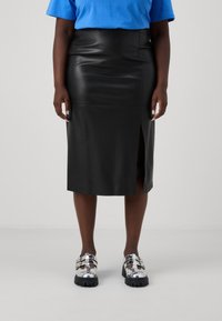 Falda midi de cuero negro con una abertura lateral, textura suave, combinada con zapatos de plataforma plateados con hebillas y suela gruesa.