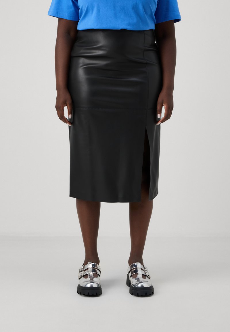 Falda midi de cuero negro con una abertura lateral, textura suave, combinada con zapatos de plataforma plateados con hebillas y suela gruesa.
