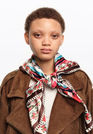 Joven con cabello corto y rizado que lleva una chaqueta de ante marrón y una bufanda de seda floral colorida atada alrededor del cuello.