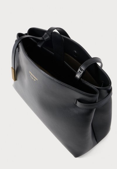 Μαύρη δερμάτινη τσάντα tote με διπλές λαβές στην κορυφή, ανοιχτό σχεδιασμό και χρυσότυπη διακοσμητική λεπτομέρεια στο πλάι. Λείος υφή, μινιμαλιστικό στυλ.