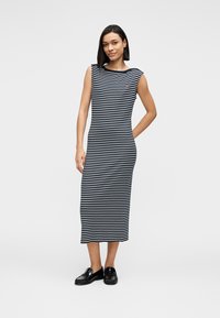 Ριγέ αμάνικο φόρεμα σε ναυτικό μπλε και λευκό με χαλαρή εφαρμογή, που φτάνει μέχρι το μέσο της γάμπας. Φορεμένο με μαύρα παπούτσια τύπου slip-on. Λείο βαμβακερό ύφασμα.