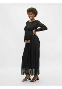 Robe de maternité noire avec des manches longues en dentelle, corsage ajusté et jupe fluide. Conçue pour le confort, elle comporte une taille élastique et des accents transparents.