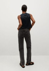 Top senza maniche nero, jeans grigi a vita alta e sandali neri. I jeans hanno una texture sbiadita, tasche posteriori e un taglio dritto.