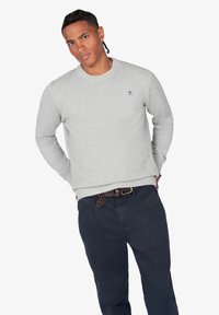 Suéter texturizado gris claro con cuello redondo, combinado con pantalones azul oscuro. Presenta un pequeño logo azul en el pecho y puños acanalados.